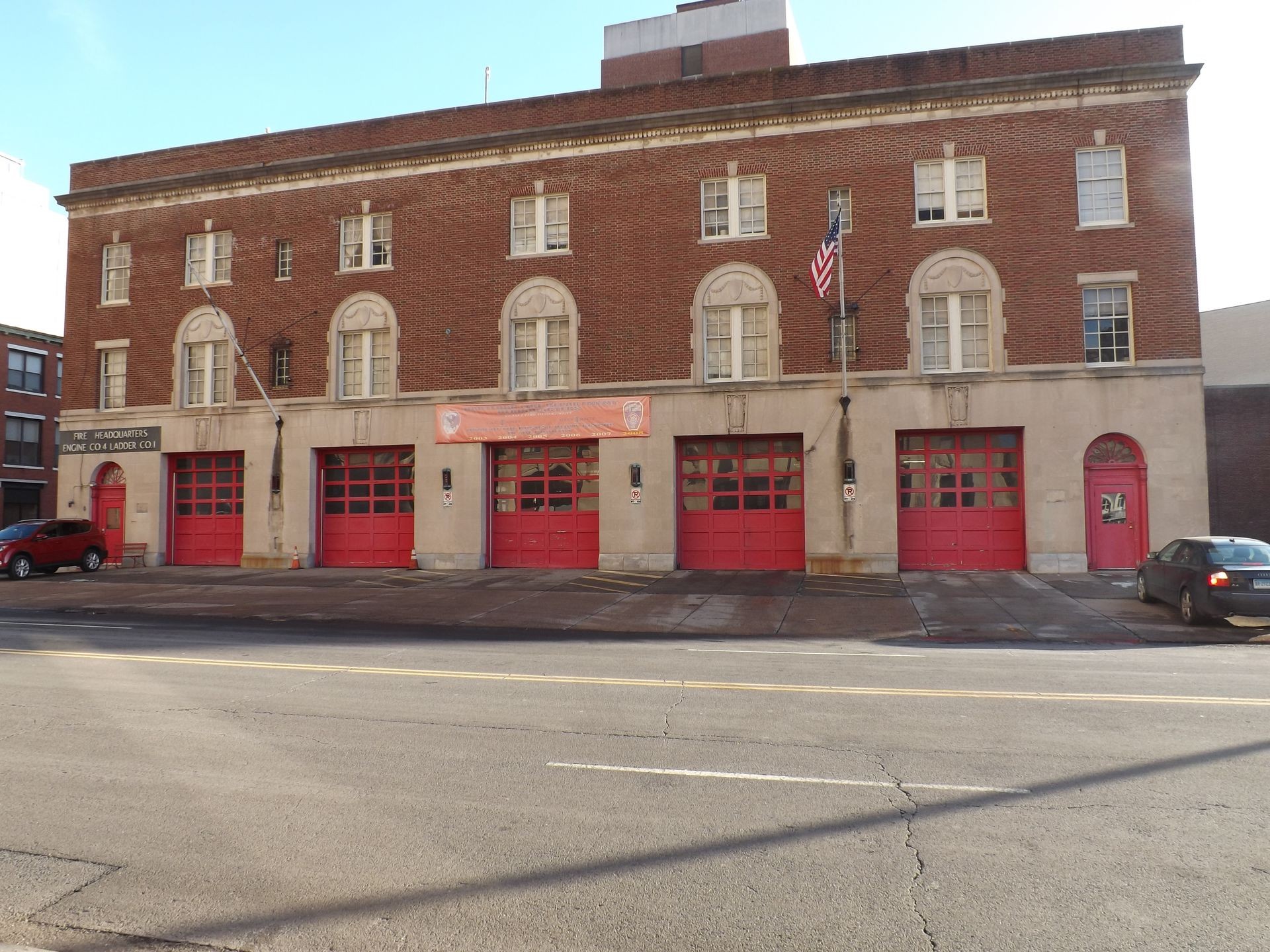 Exterior view of a fire station with red garage doors and an American flag on the facade.