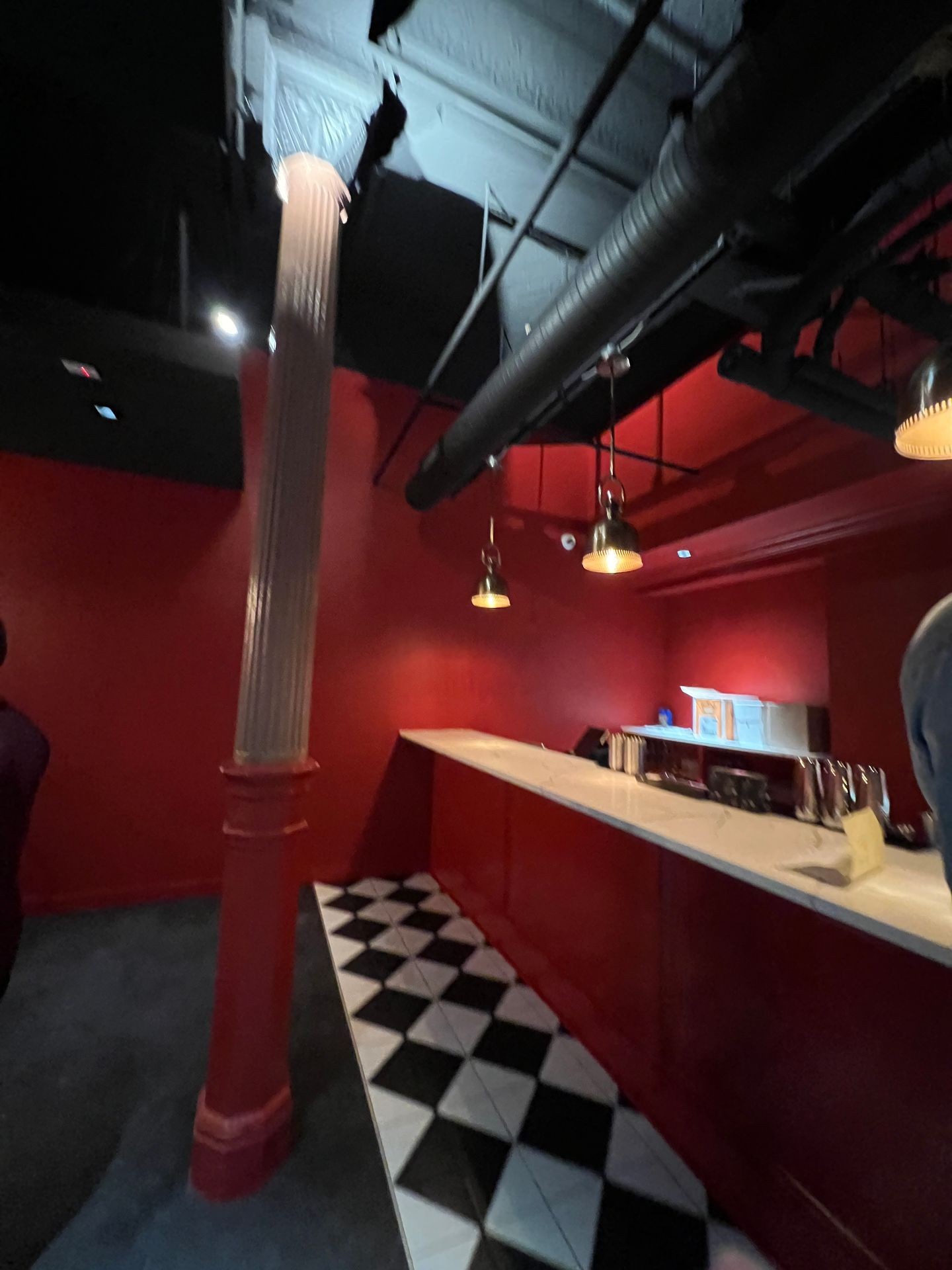 Dimly lit red interior with a column, checkered floor tiles, and decorative ceiling pipes.