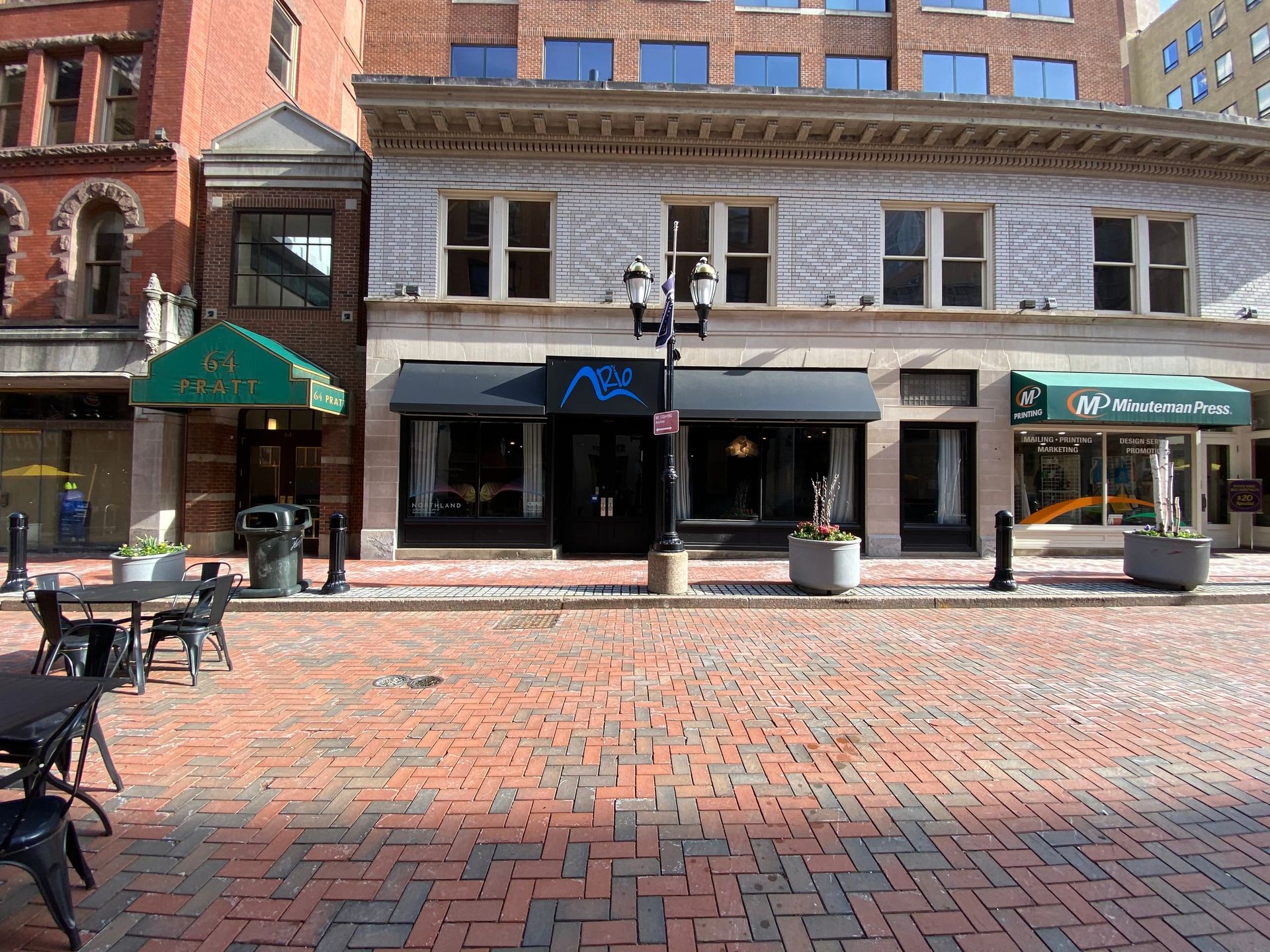 Street view of buildings with awnings, brick pavement, and empty outdoor seating area.